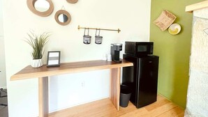 Cocina compacta con cubierta de madera, refrigerador negro y microondas. Hay tres espejos montados en la pared y una pequeña planta en maceta a la izquierda.