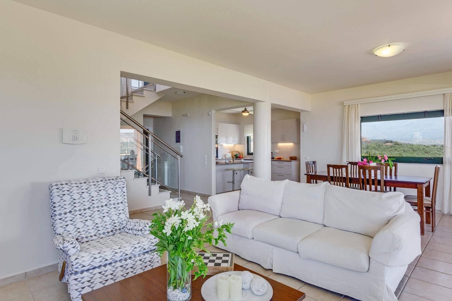 Uma sala de estar moderna com um sofá, poltrona estampada e um espaço de refeições com mesa e cadeiras.