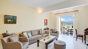 Un salon spacieux comprenant un canapé, des fauteuils, une table basse et un coin repas offrant une vue sur la mer.