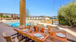 Un espace repas avec vue sur la piscine, des sièges d’extérieur et une table préparée pour le petit-déjeuner.