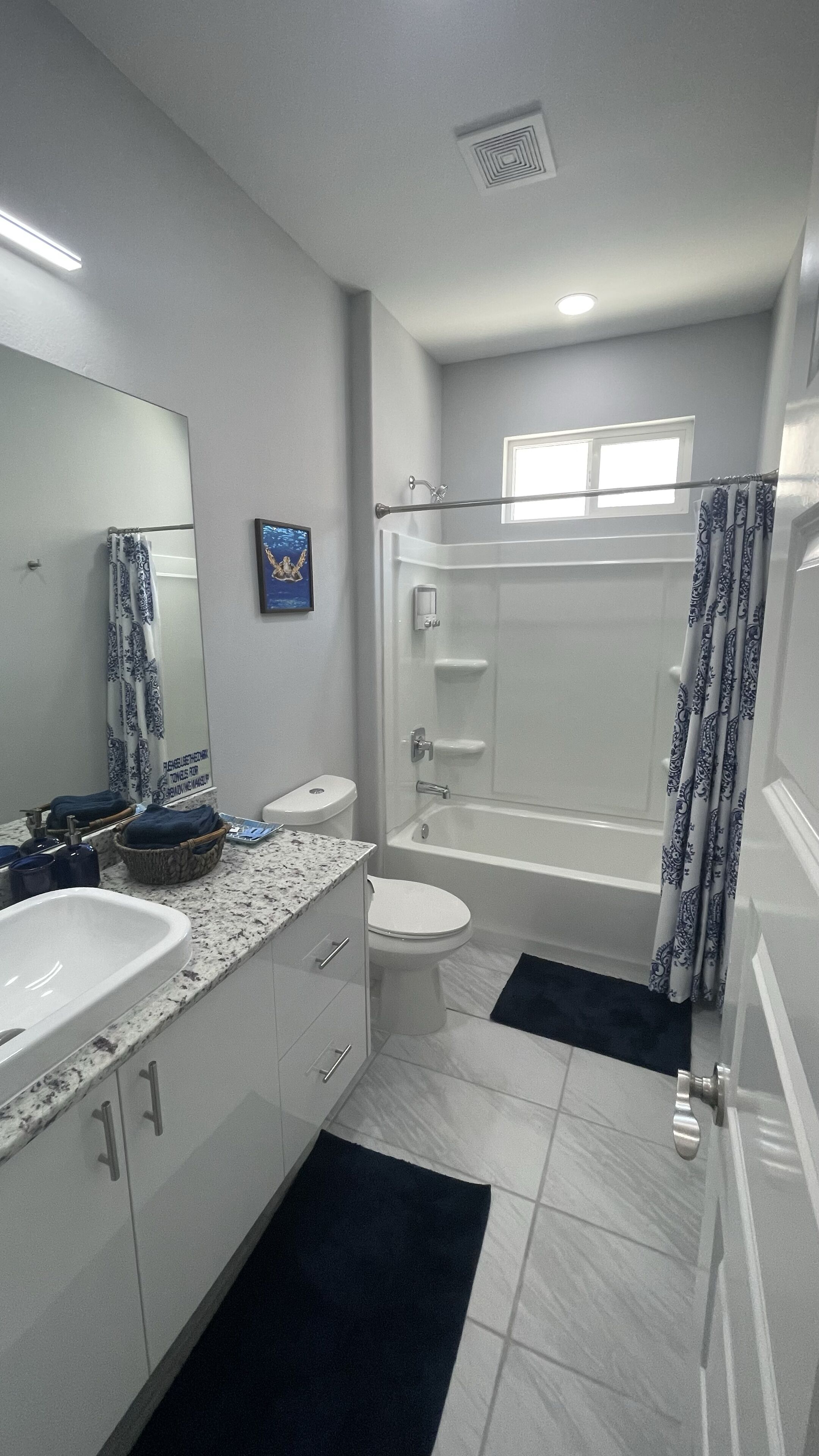 Un baño moderno con un lavamanos, inodoro y bañera blancos. Hay una cortina de ducha, un perchero y un espejo en la pared.