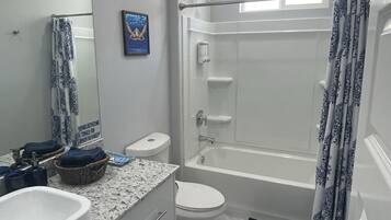 Un baño moderno con un lavamanos, inodoro y bañera blancos. Hay una cortina de ducha, un perchero y un espejo en la pared.