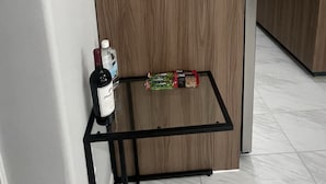 Una cuina amb un armari de fusta, una placa daurada amb la inscripció "CHAMPAGNE lounge", una prestatgeria de metall negre amb una ampolla de vi i dos envasos de llaminadura, i un frigorífic.