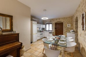 A dining area with a glass table, white chairs, and a stone wall.