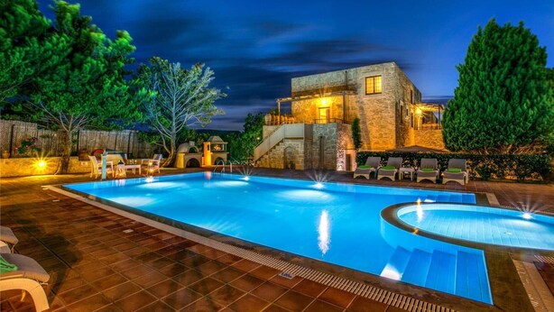 A swimming pool with a stone building in the background, surrounded by trees and a wooden deck. - Villa Minos by Villa Plus (Agia Pelagia)
