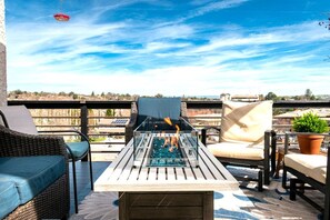 Un patio al aire libre con una mesa de vidrio, mobiliario de mimbre y vistas a la ciudad.