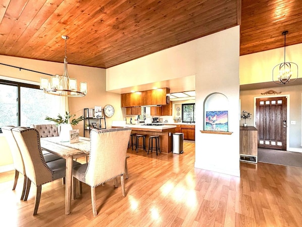 Una cocina amplia con armarios de madera, un comedor con mesa y sillas, y una vista a través de un arco hacia otra habitación.