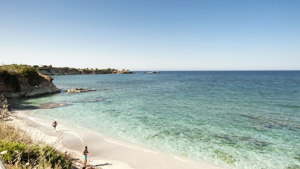 A beach with clear turquoise water, a sandy shore, and rocky cliffs in the background. - Villa Monroe by Villa Plus (Hersonissos)