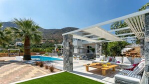 A modern outdoor living area with a pool, stone pillars, and a white pergola. - Villa Monroe by Villa Plus (Hersonissos)
