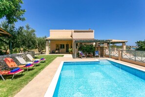 A poolside area with lounge chairs, a covered seating area, and a view of the sea.