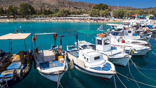A marina with several boats docked, a beach with people in the background, and a hilly landscape. - Villa Olive Grove by Villa Plus (Marathi)