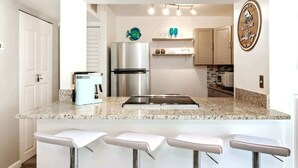 Cocina moderna con encimera de granito, electrodomésticos de acero inoxidable y taburetes de bar blancos.