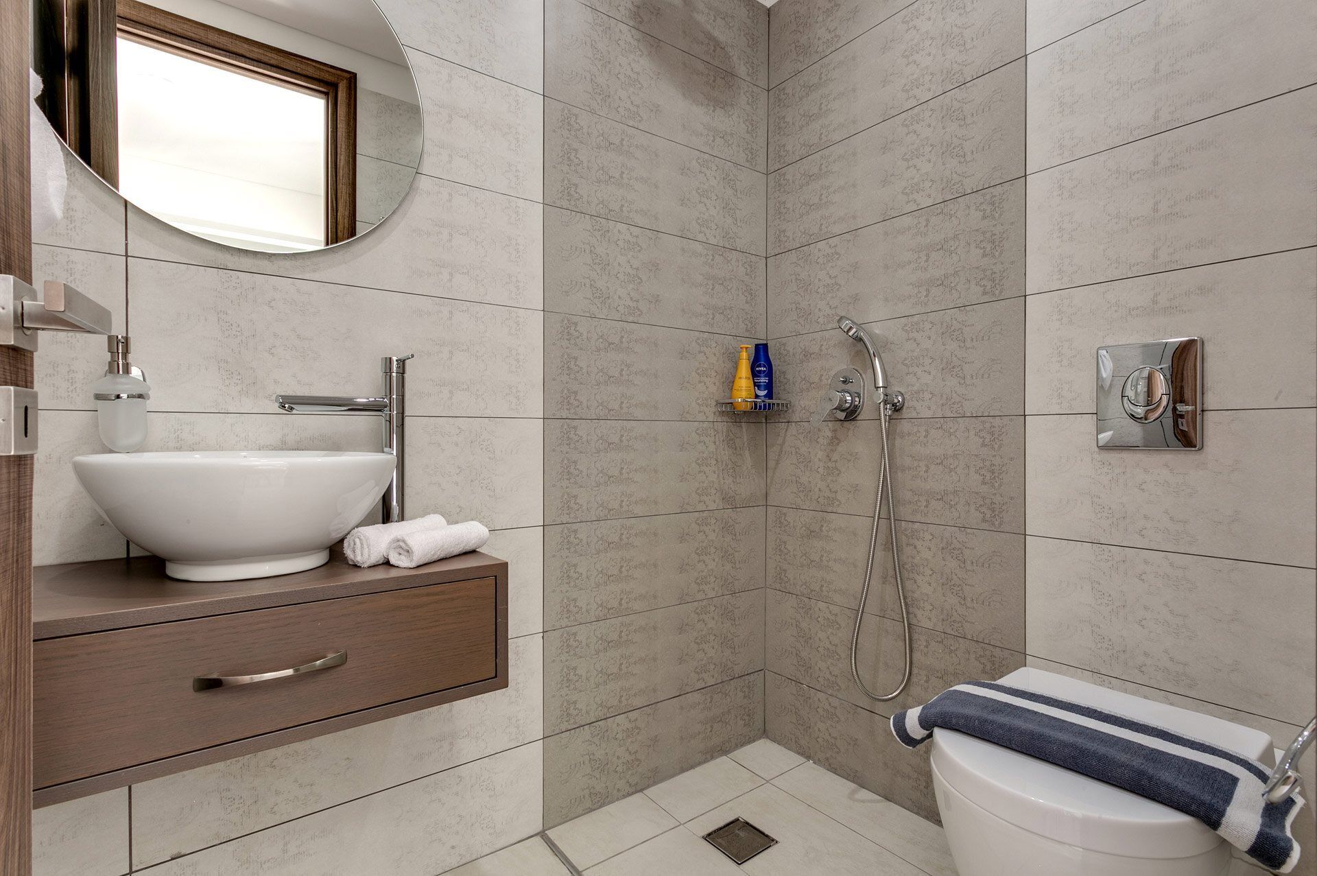 A modern bathroom with a white sink, a mirror, a shower, and a toilet.