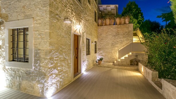 A stone building with a wooden door, a window with bars, and a staircase leading to an upper level. - Villa Vincenzos by Villa Plus (Agia Pelagia)