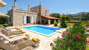 Una casa a due piani con piscina, pareti in pietra e un giardino fiorito e ricco di piante.