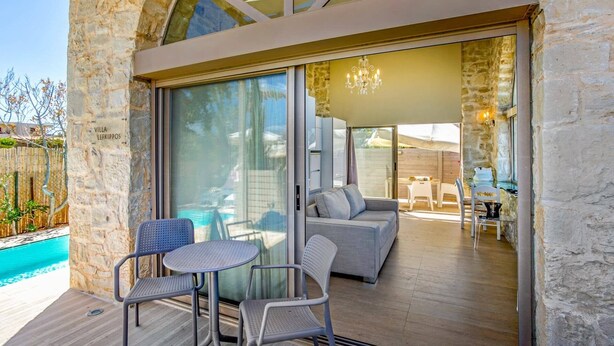 Eine Villa mit Glastür, die auf einen Sitzbereich mit Pool im Freien führt.