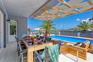 Un espace extérieur abrité, aménagé pour les repas, avec une piscine et des chaises longues.