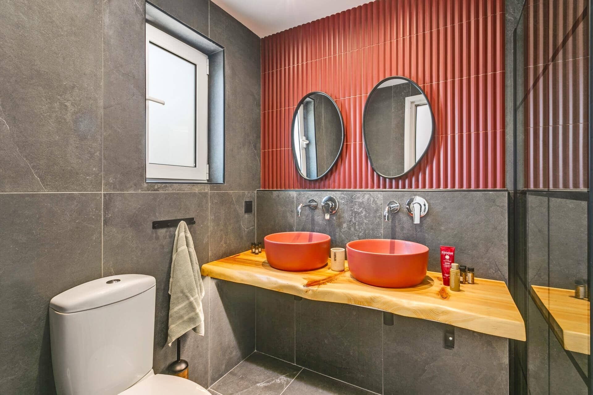 Un bagno con due specchi rotondi, un mobile vanitario in legno e un water.