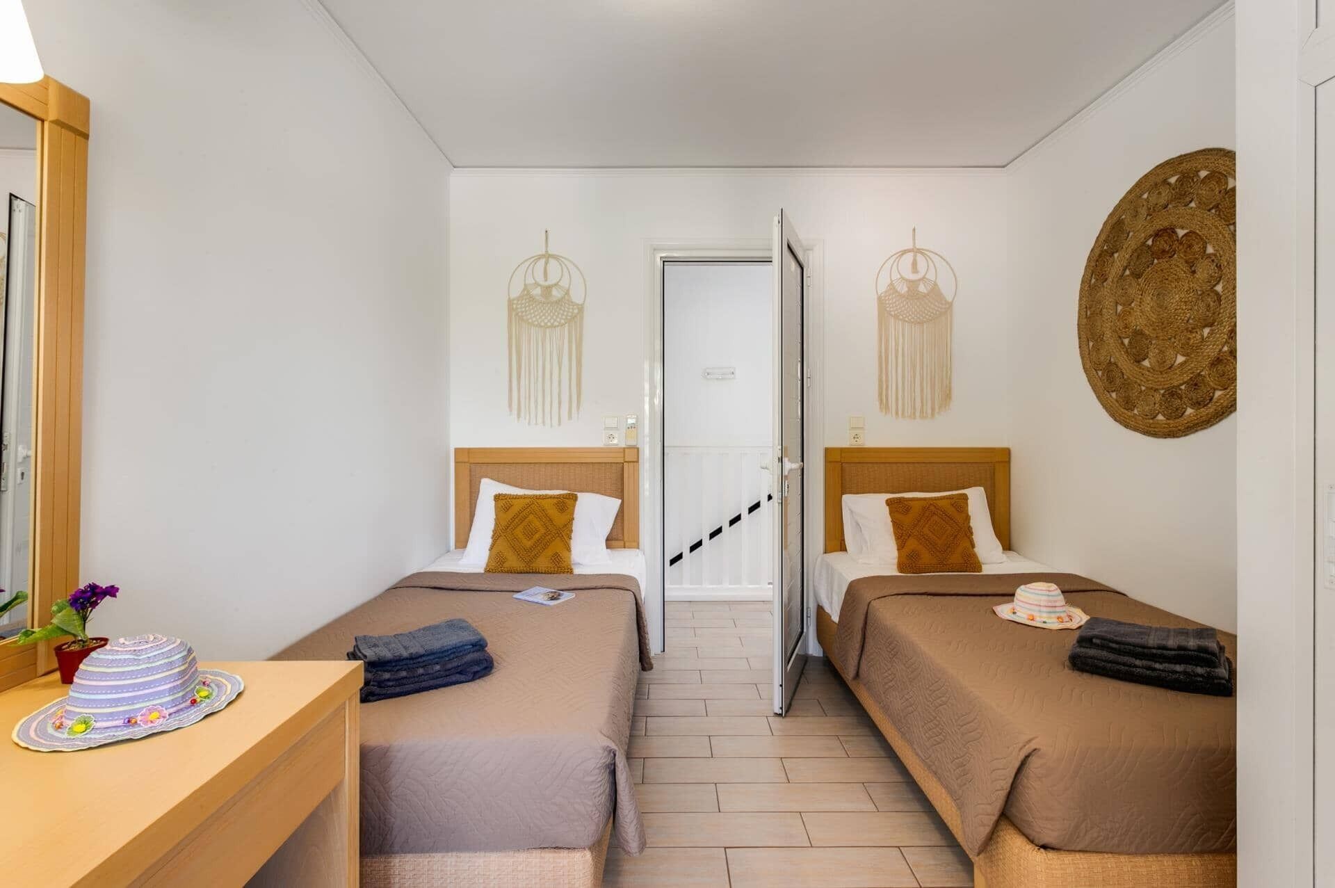 Quarto com duas camas, uma escrivaninha de madeira, um espelho e uma porta que dá para outro cômodo.
