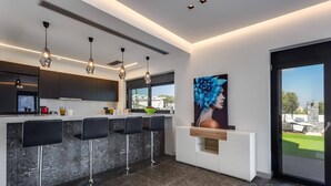 A modern kitchen with a bar area, pendant lights, and a large window. - Villa Tropicana by Villa Plus (Hersonissos)
