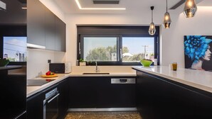 A modern kitchen with black cabinetry, a built-in dishwasher, a microwave, and a window with a view of the city. - Villa Tropicana by Villa Plus (Hersonissos)