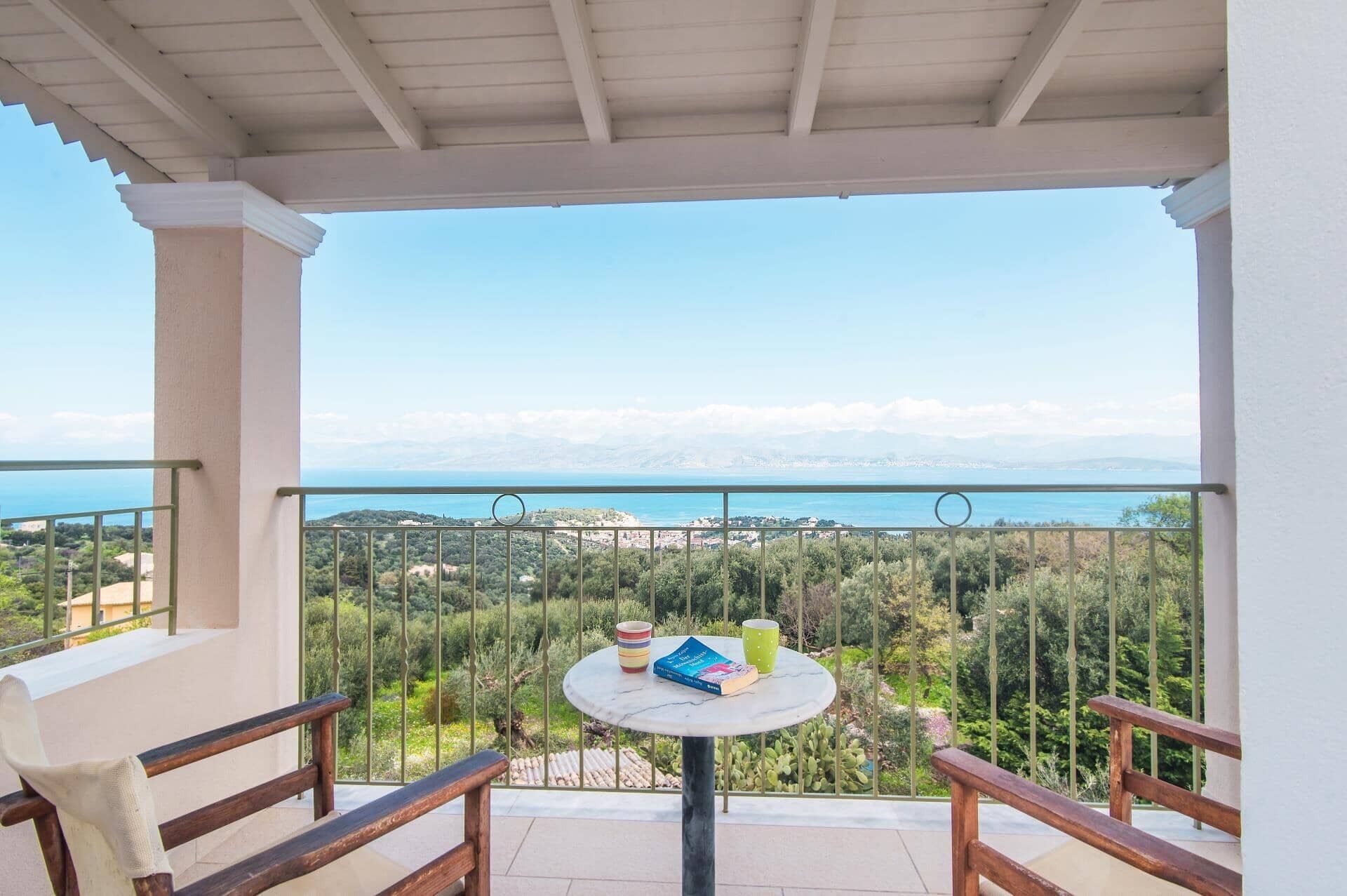 Ein Balkon mit Tisch, Stühlen und Blick auf das Meer und die Berge.