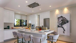 Een moderne keuken met een centraal eiland, barkrukken en een groot raam.