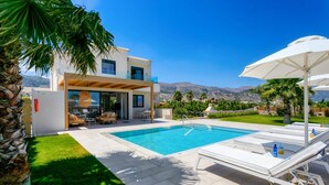 A modern poolside area with a clear blue pool, lounge chairs, and umbrellas. - Villa Mariba White by Villa Plus (Malia)