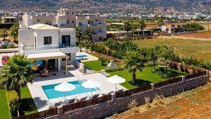 A modern hotel with a swimming pool, outdoor seating, and a view of the surrounding landscape. - Villa Mariba White by Villa Plus (Malia)
