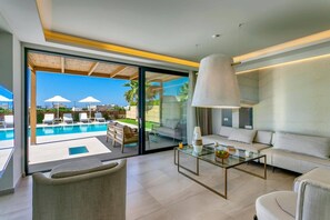 Una sala de estar moderna con una mesa de centro de vidrio, un sofá y vistas a una piscina y zona de estar exterior.