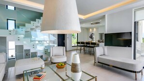 A modern living room with a glass coffee table, white sofas, and a large TV. - Villa Mariba White by Villa Plus (Malia)
