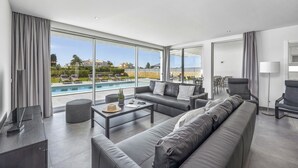 A modern living room with a large pool, grey furniture, and a view of the surrounding landscape. - Villa Casa Magnolia by Villa Plus (Vale Rebelho)