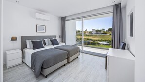 A modern bedroom with a large bed, a desk, and a view of a landscaped area. - Villa Casa Magnolia by Villa Plus (Vale Rebelho)