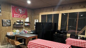 A restaurant with a Super Bowl LII banner, a kitchen area with a refrigerator and stove, and two tables with red and white checkered tablecloths. - Cabin 9 - Rustic Mountain Cabin Rental - Up to 3 persons (Hatfield)