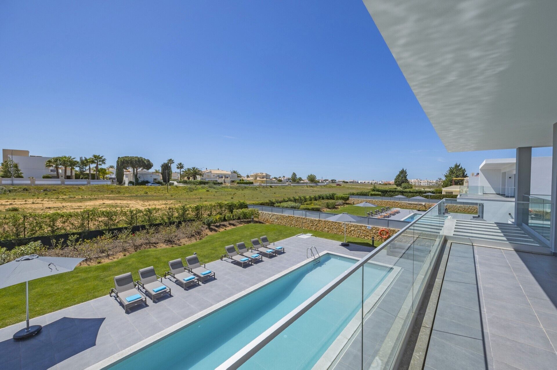 Un espace piscine moderne offrant une vue dégagée sur le paysage environnant, notamment un champ verdoyant et des bâtiments situés au loin.