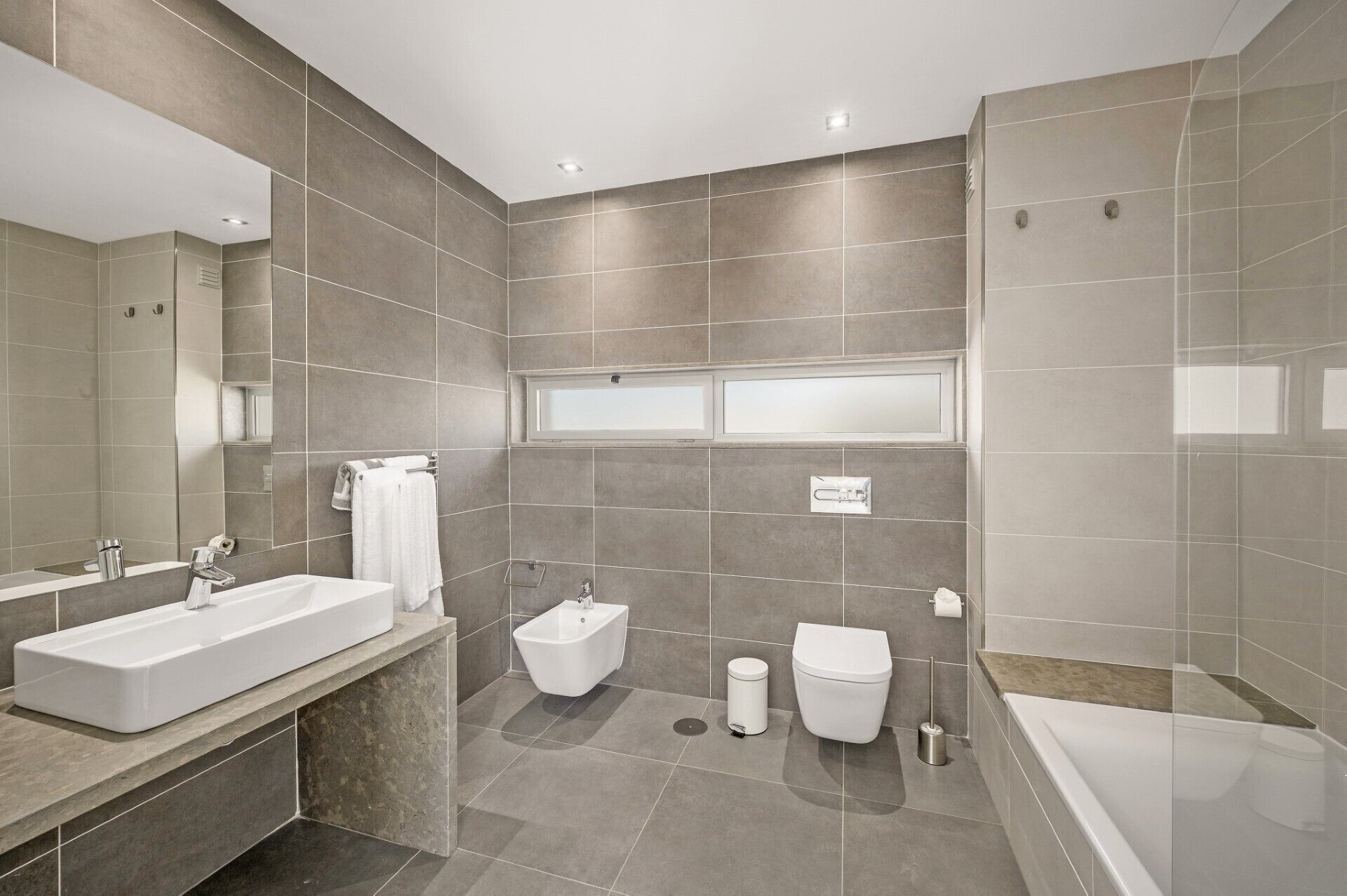 A modern bathroom with a large mirror, a bathtub, a toilet, and a bidet.