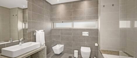 A modern bathroom with a large mirror, a bathtub, a toilet, and a bidet.