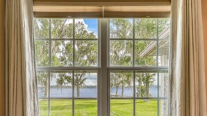 Una ventana con vistas a un lago, rodeado de árboles y un espacio cubierto de césped.
