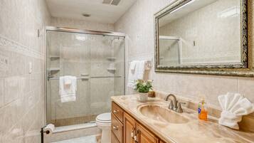 A bathroom with a glass-enclosed shower, a sink with a mirror, and a toilet.