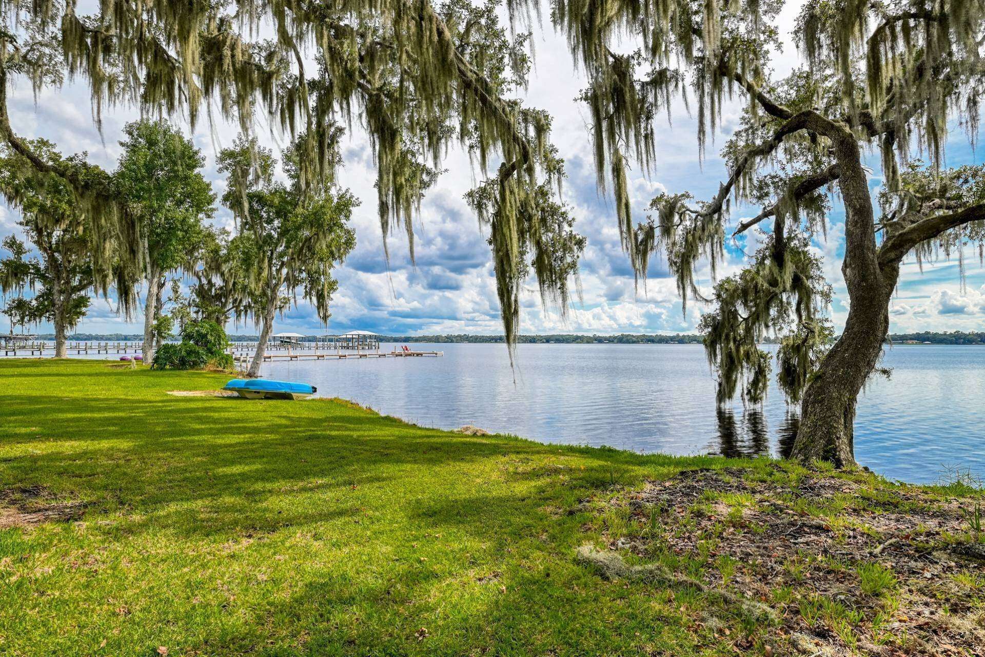 Vista de un lago con una zona verde, un muelle y un bote.