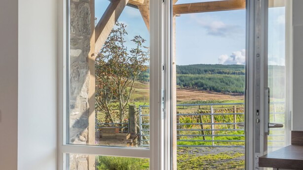 A room with a large window, stone wall, and a view of a rural landscape with fields and trees.