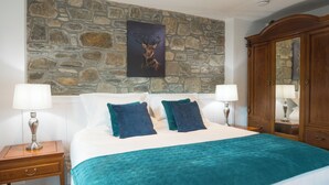 A bedroom with a stone wall, a bed with teal bedding, two bedside tables with lamps, and a wooden wardrobe.