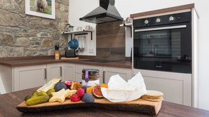 A kitchen with a stone wall, a hanging picture, a modern oven, and a wooden board with various foods.