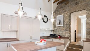 A modern kitchen with white cabinetry, a wooden island, and a stone accent wall.