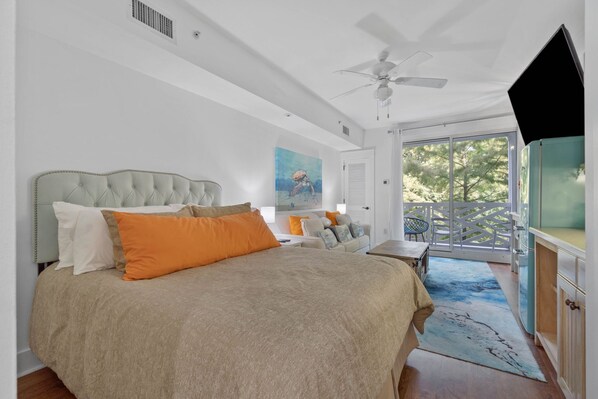 A bedroom with a large bed, a ceiling fan, a painting on the wall, and a view of the outdoors. - Easy Breeze on Bay 423–Colorful–Sleeps 3 (Miramar Beach)