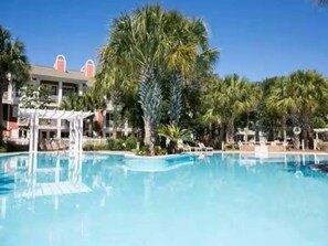 A swimming pool surrounded by palm trees and a building with a covered outdoor area. - Easy Breeze on Bay 423–Colorful–Sleeps 3 (Miramar Beach)