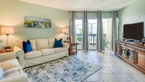 A living room with a beige sofa, two lamps, a flat-screen TV, and a patterned rug. - Island House C219 (St. Augustine)