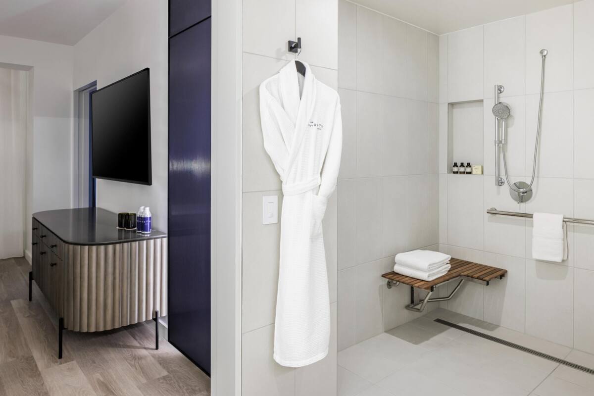 A modern bathroom with a shower, a towel rack, a vanity with a mirror, and a flat-screen TV.