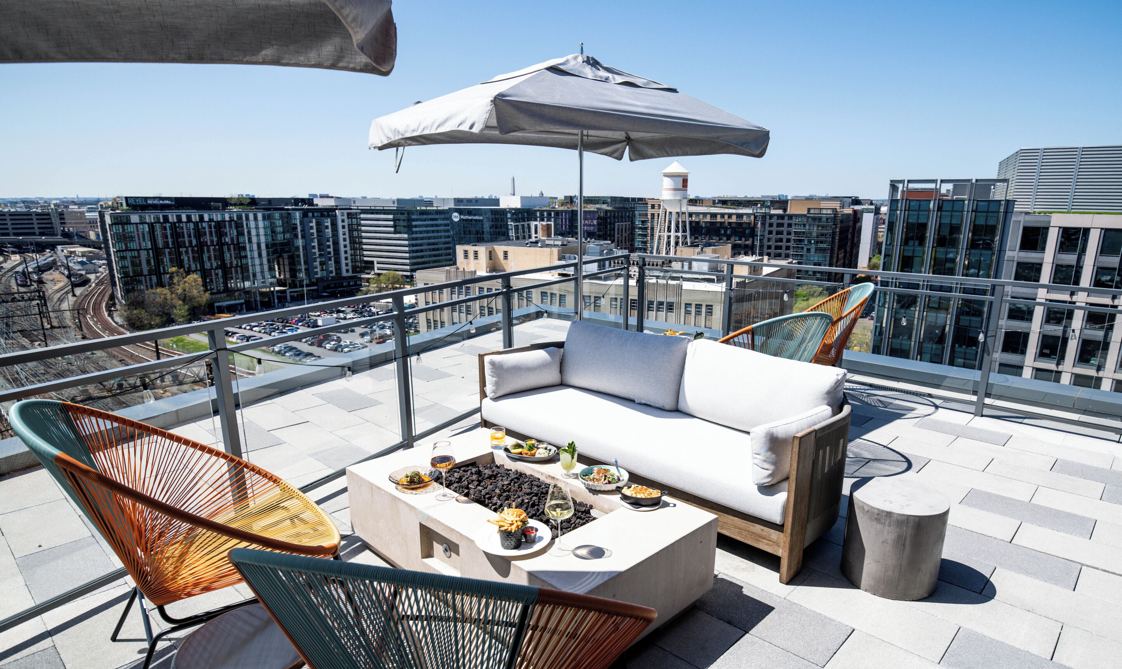 A rooftop terrace with a sofa, chairs, a table with food, and a large umbrella.