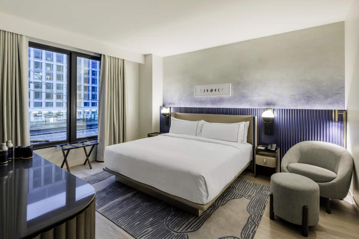 A modern hotel room with a large bed, bedside tables, a desk, and a chair.